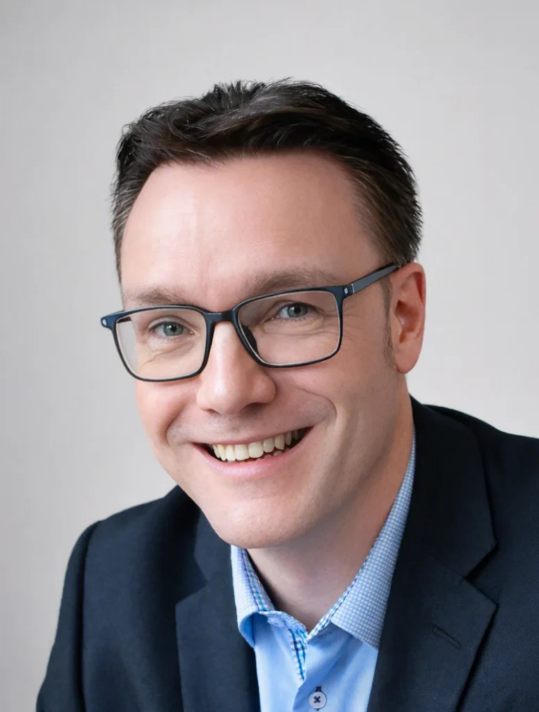 A smiling man wearing glasses and a suit jacket poses for a professional portrait.