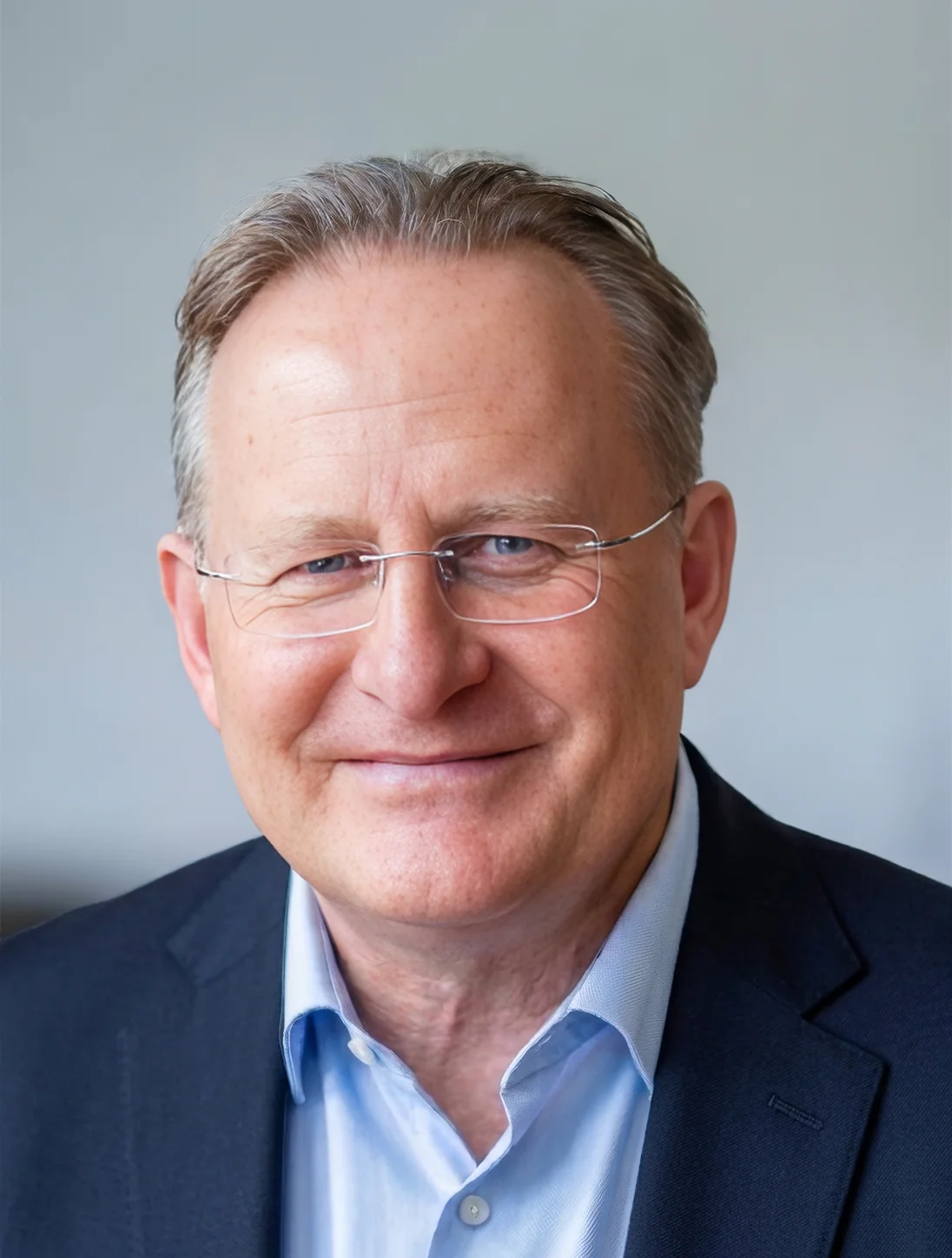 A portrait of a smiling man in a suit and glasses.