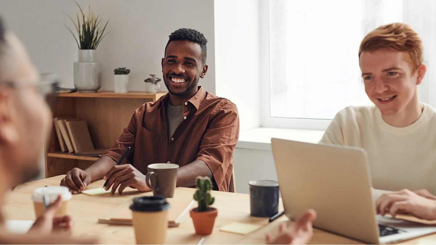A diverse team meeting in an office with smiling individuals around a table.