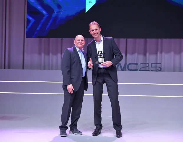 Two men on stage at the MWC25 event, one of them holding an award.