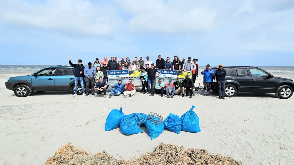 A group photo of a team on the beach after a cleanup, with blue bags of collected trash in the foreground.
