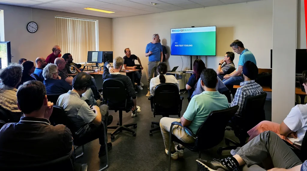 A group of people attentively listens to a presentation in an office meeting room.